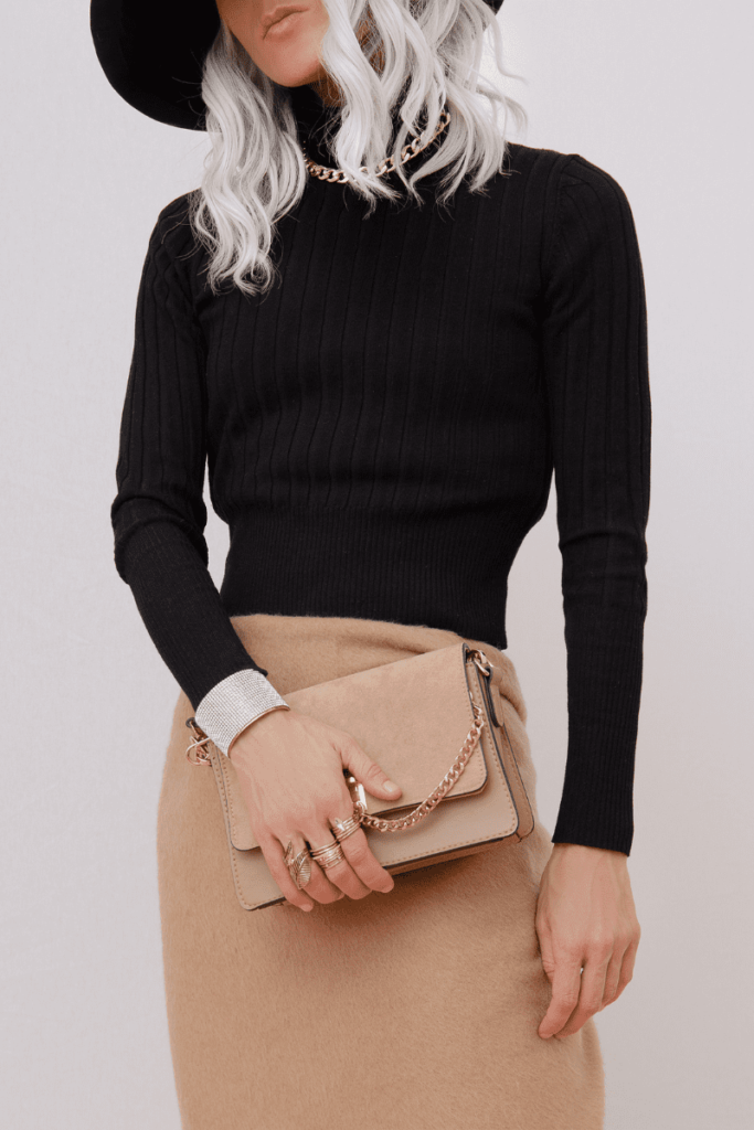Woman dressed in a chic casual outfit, featuring a black turtleneck, neutral skirt, and carrying a stylish hand purse.
