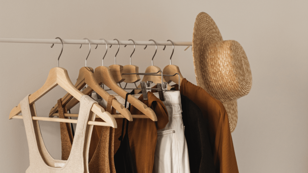 Assorted clothing items and a straw hat displayed on a hanging rack