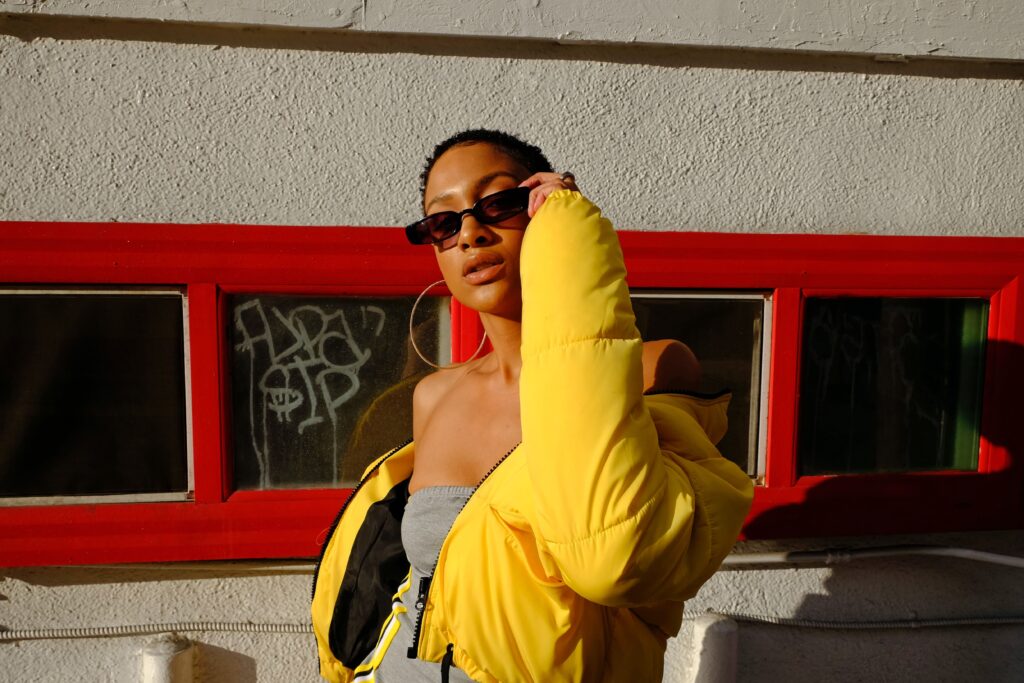 Girl sporting a yellow cropped puffer jacket on the street, striking a pose with her black sunglasses.