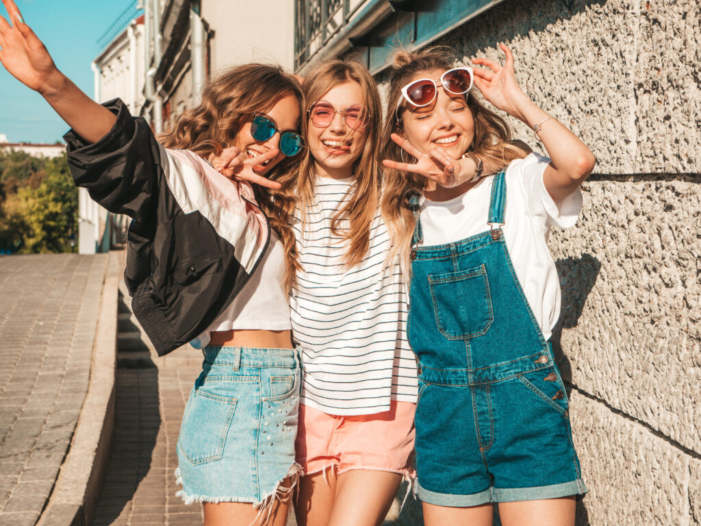 Portrait of confident, carefree women showcasing outfit ideas, posing near a wall on the street, radiating positivity and having fun in sunglasses.
