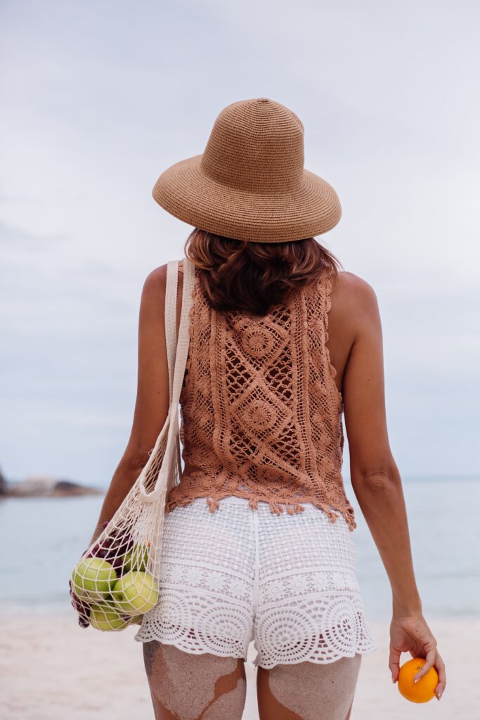 Attractive, tanned, and fit young Caucasian woman wearing knitted clothes and a hat while enjoying her time on the beach.