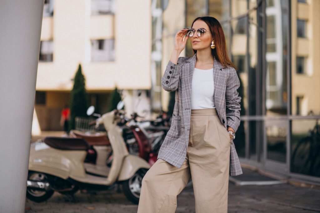 Young woman in a stylish suit standing next to a scooter.