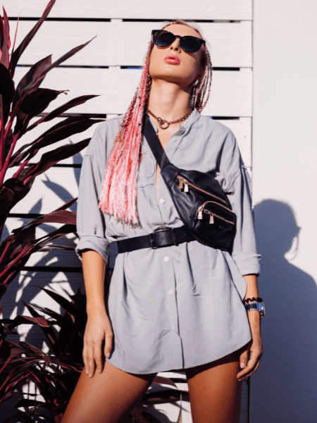Young stylish woman with pink purple braids and black waist bag posing outdoor
