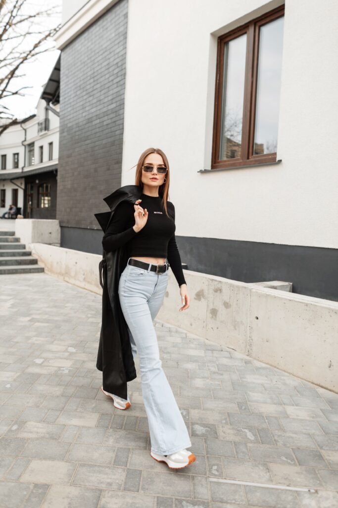 Fashionable, confident girl in vintage sunglasses, black t-shirt, high waist flare jeans, and coat strolling through the city