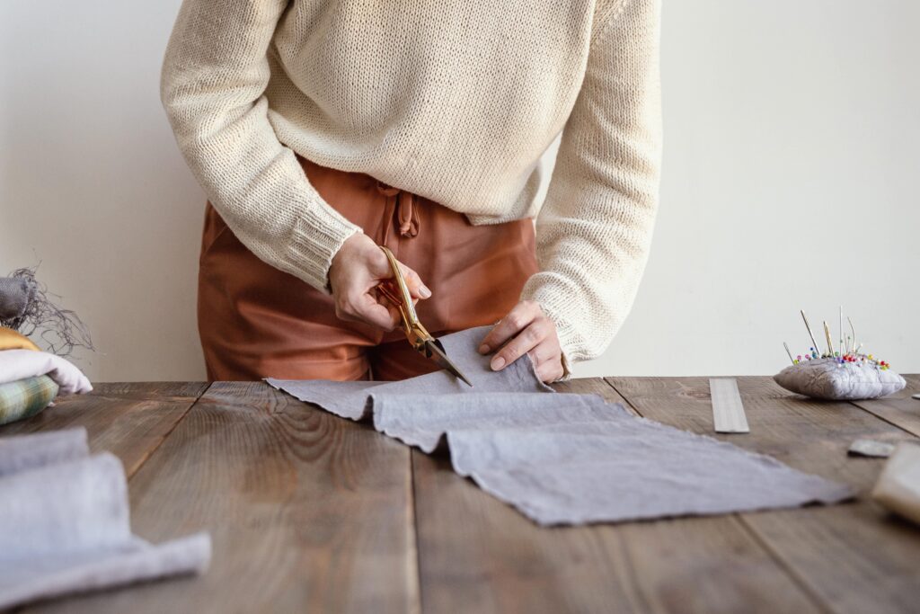 A photo of a woman upcycling clothes by cutting fabric with scissors.
