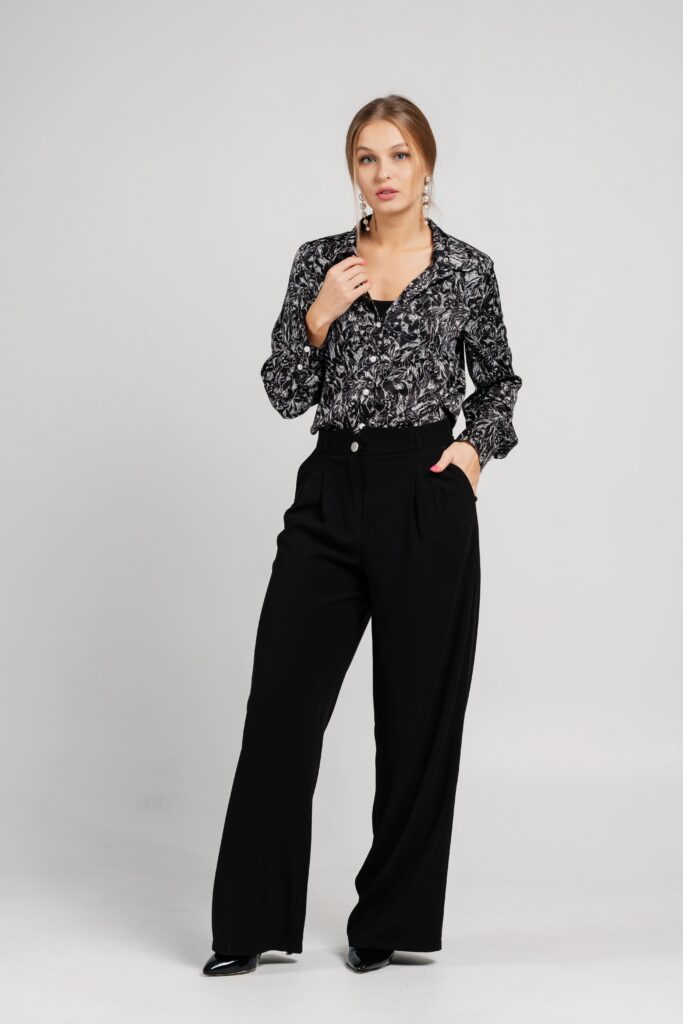 This is a studio portrait of a woman wearing a blouse and trousers.