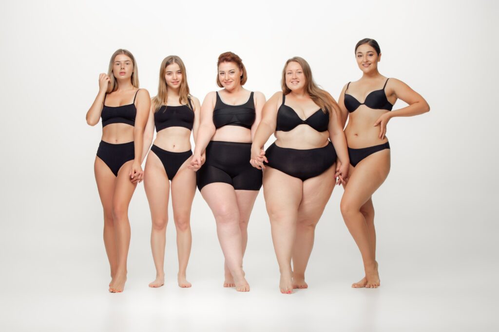 Image of a group of attractive young women with diverse body types posing together on a white background.