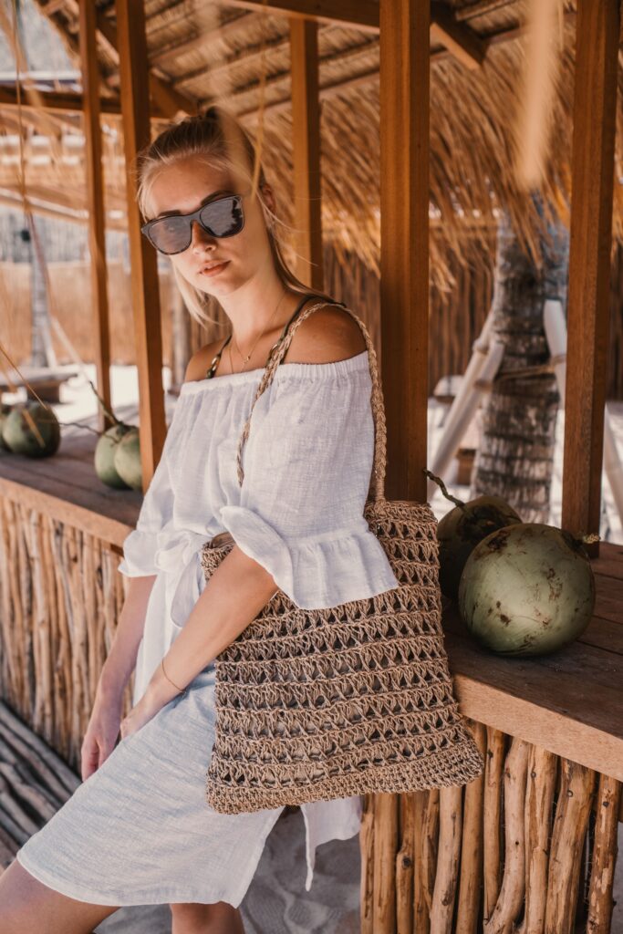Woman wearing sustainable white summer attire, posing near a wooden café
