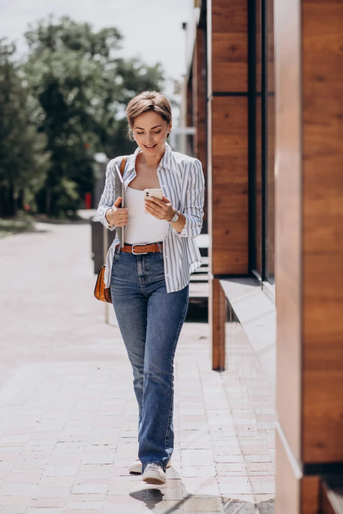 Young Woman Embracing Casual Style: Free Photo of Her Walking on the Street with Phone and Computer