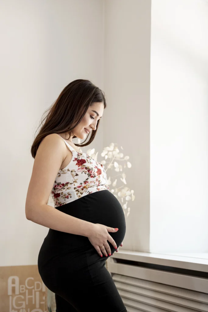 Pregnant woman in side view showcasing trimester-specific maternity style while gently holding her belly