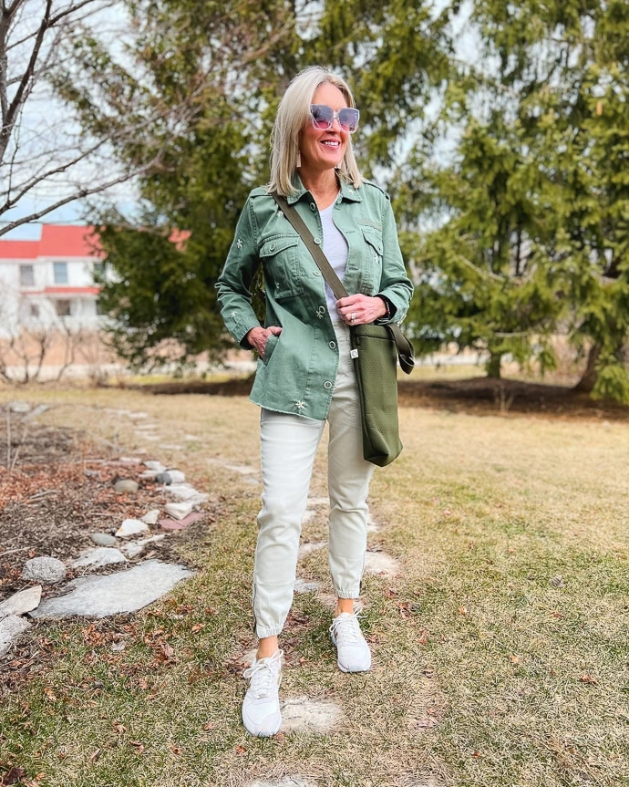 An image showcasing a woman in white pants and sneakers, paired with a white shirt and an olive-green long sleeve shirt, demonstrating the concept of layering for both style and comfort during St. Patrick's Day.