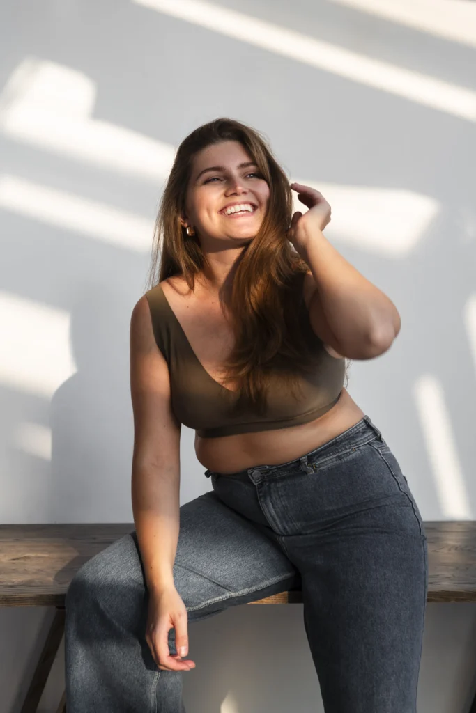 Happy woman confidently showcasing her figure in blue jeans and a brown sports bra.