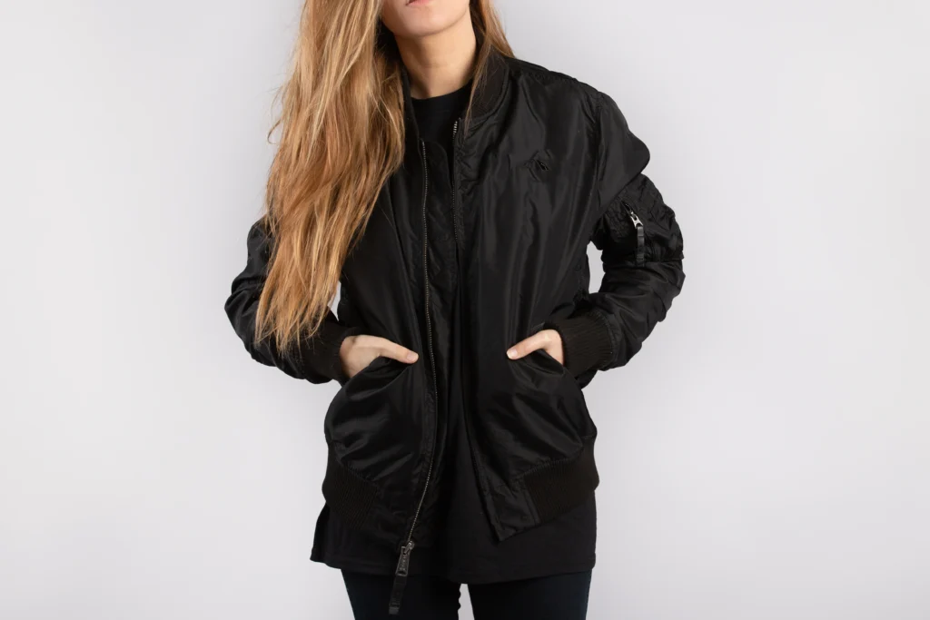 Young woman in a minimalist black jacket posing against a clean white wall, exemplifying Seasonal Minimalist Wardrobe Transition.
