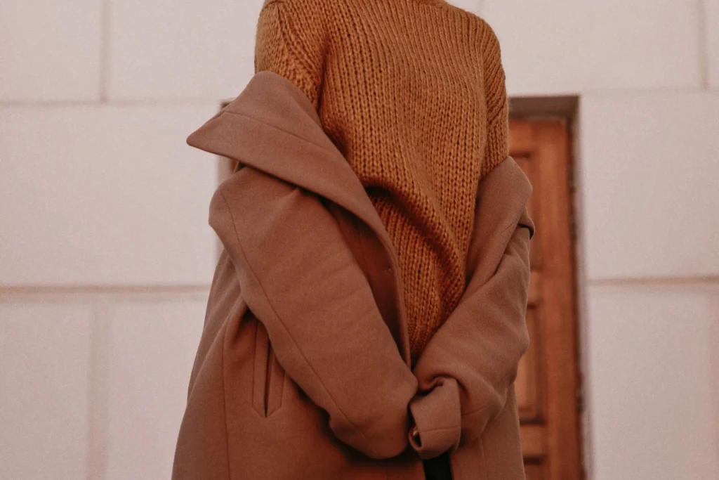 Woman in neutral-toned knit sweater and long coat outdoors.