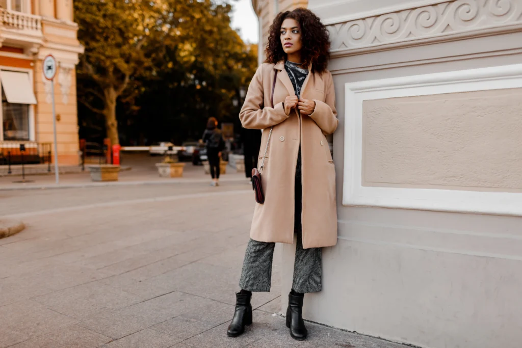 Outdoor fashion portrait of glamour sensual young stylish black lady wearing trendy fall outfit, grey velvet sweater and beige wool coat.