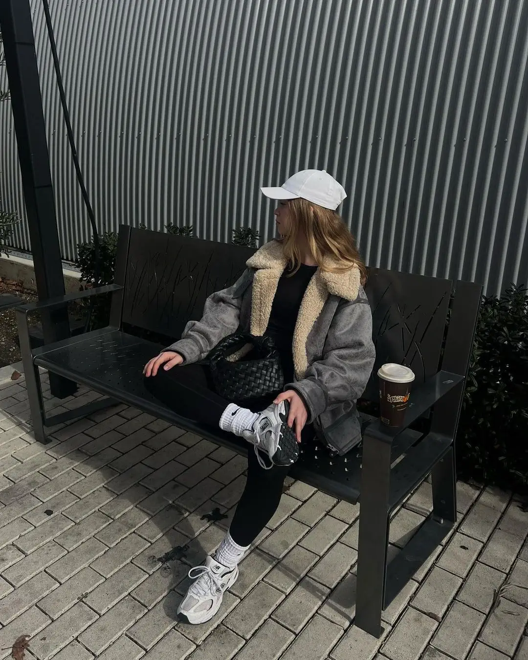 Girl siting wearing a fashionable gym outfit with white hat, leggings and a wool jacket