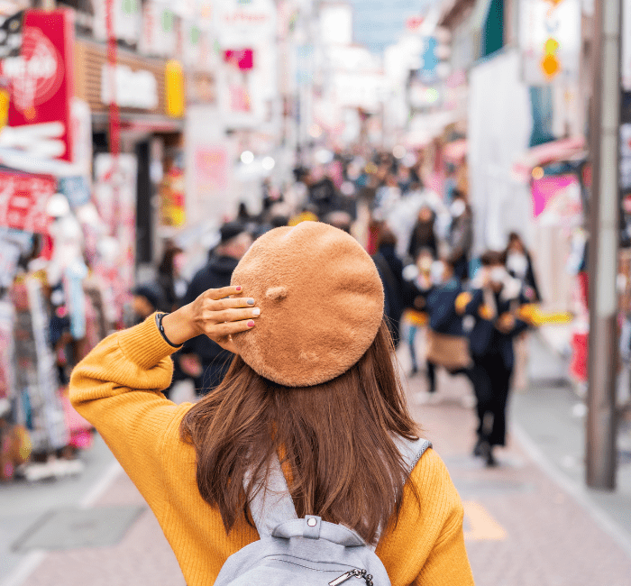 Young woman traveler in versatile clothing for travel, exploring Harajuku's Takeshita Street, the center of teenage fashion and cosplay culture in Tokyo