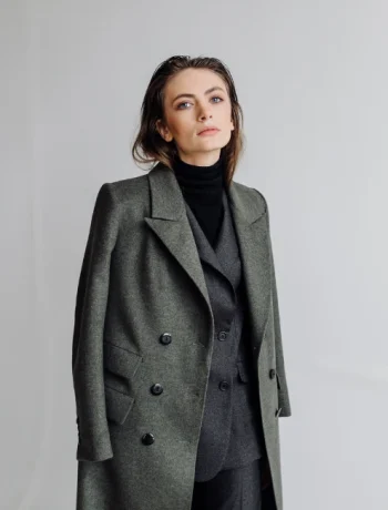 A woman embodying minimalist style, dressed in a black turtleneck, dark gray suit, and lighter gray jacket, demonstrating the art of color coordination and simplicity in fashion. Her ensemble reflects a monochromatic color palette, typical of a minimalist wardrobe, underlining the principles of sustainable and conscious fashion.