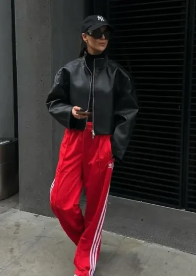 Lady showcasing her athleisure workplace dos and don'ts outfits with a black hat, black leather jacket, t shirt, and a red sports trousers, with white sneakers