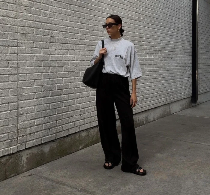 Minimalist style influencer Natalie Helen pulling off a casual dress code outfit wearing a darb pants with gray shirt, sunglasses, tote bag and slippers