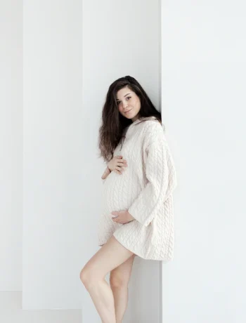 Expectant brunette woman showcasing maternity style in a comfortable oversized knitted sweater.