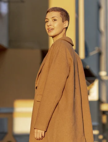 Lady with short hair smiling in a trench coat, looking at the sunrise – Minimalist Outerwear for fall.