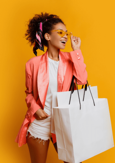 Studio shot of a beautiful black woman holding a white shopping bag, standing against a yellow background, embodying a trendy spring look and providing a visual shopping guide inspiration.