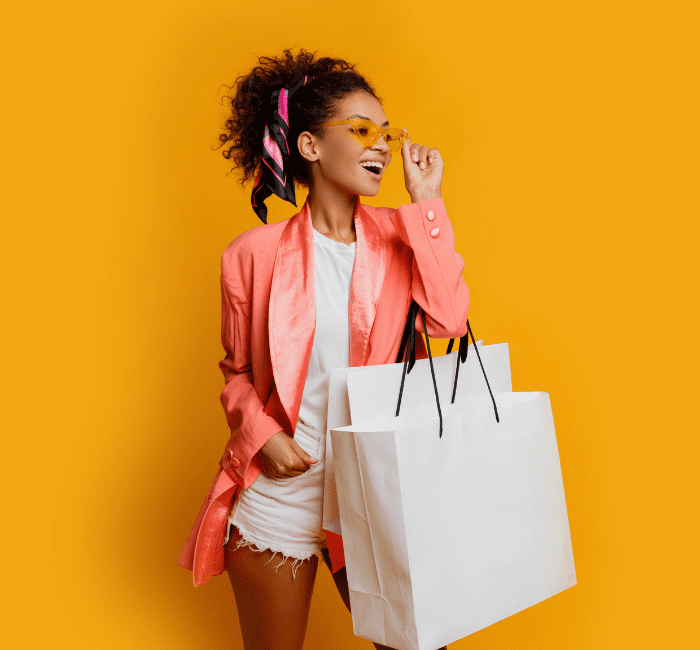 Studio shot of a beautiful black woman holding a white shopping bag, standing against a yellow background, embodying a trendy spring look and providing a visual shopping guide inspiration.