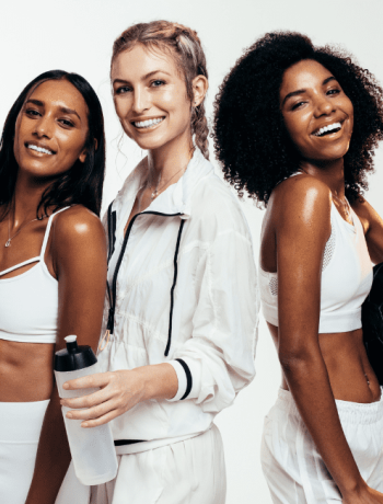 Women taking break after workout session in studio. Group of females in sportswear with exercise mat, water bottle and medicine ball on white background in their workout capsule wardrobe.