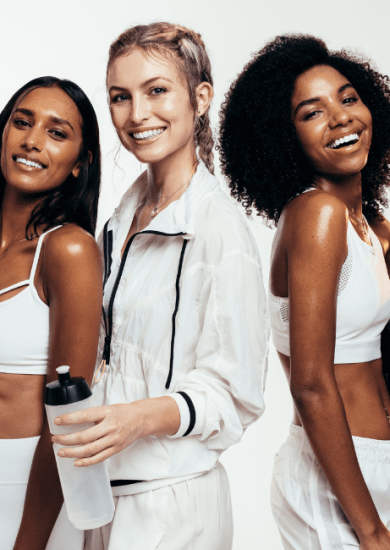 Women taking break after workout session in studio. Group of females in sportswear with exercise mat, water bottle and medicine ball on white background in their workout capsule wardrobe.